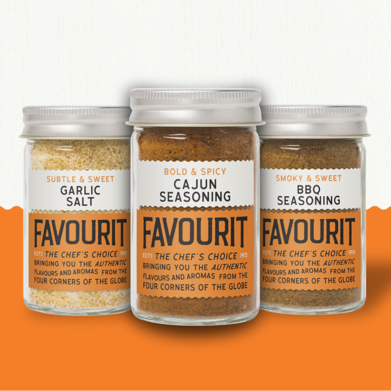 Three jars of seasonings: Garlic Salt, Cajun Seasoning, and BBQ Seasoning, placed side by side on an orange surface with a white background.