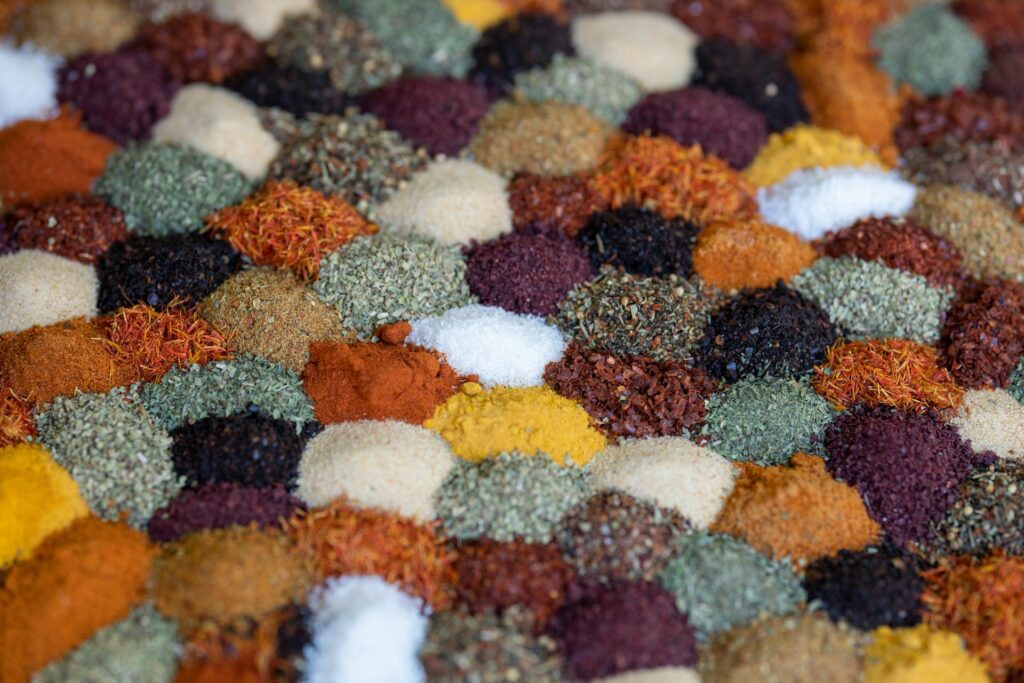 A variety of colorful herbs and spices are arranged in small, neat mounds, creating a mosaic-like pattern, perfect for enhancing your cooking with vibrant seasoning.