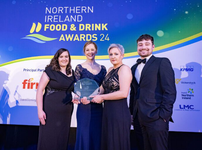 Four people in formal attire stand together on stage holding an award at the Northern Ireland Food & Drink Awards 2024.